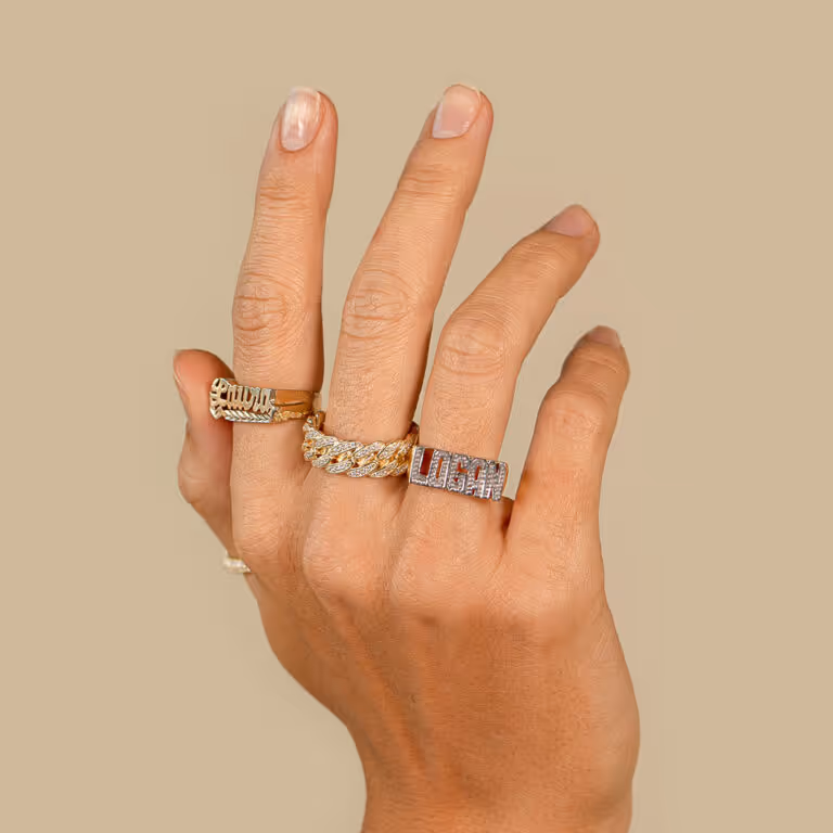 Hand wearing several gold rings against a beige backdrop
