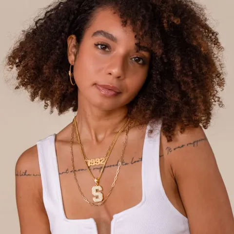 Woman with curly hair wearing a white tank top and layered gold necklaces