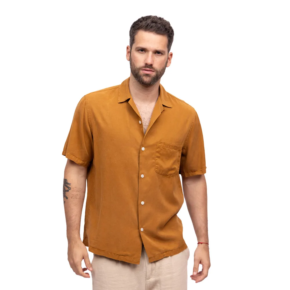 Model in an orange short-sleeve shirt and light trousers against a white background